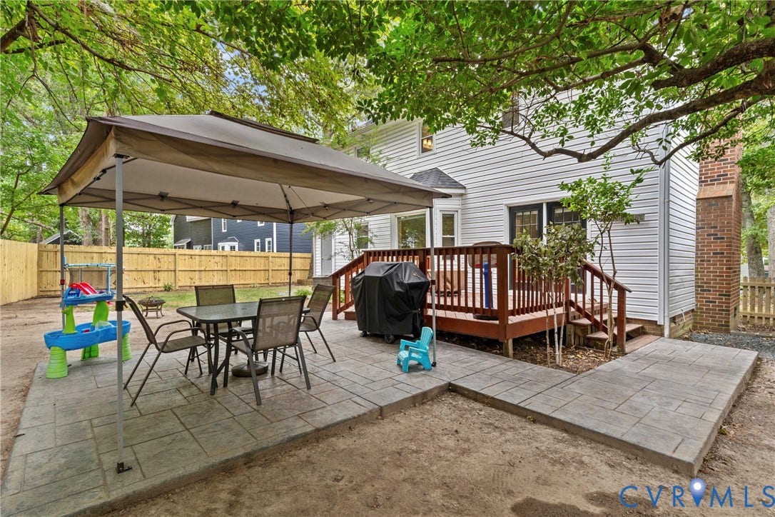 Expansive backyard featuring a wood deck with railings, an L-shaped stamped concrete patio, a brick chimney, and white siding