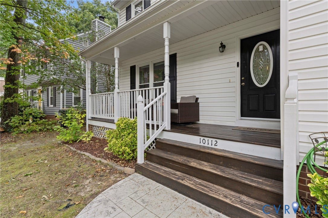 Front porch featuring wood-finish steps and flooring, white railing, and a black entry door with an oval leaded glass insert