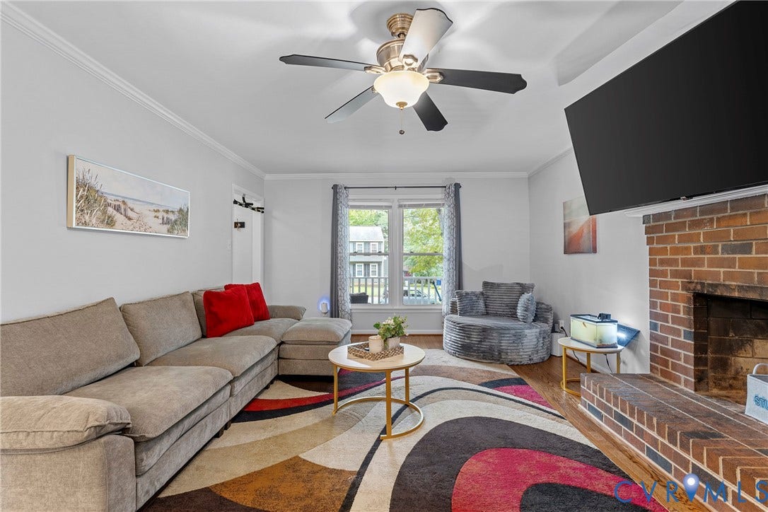 Hardwood flooring, ceiling fan with light fixture, brick fireplace, and crown molding