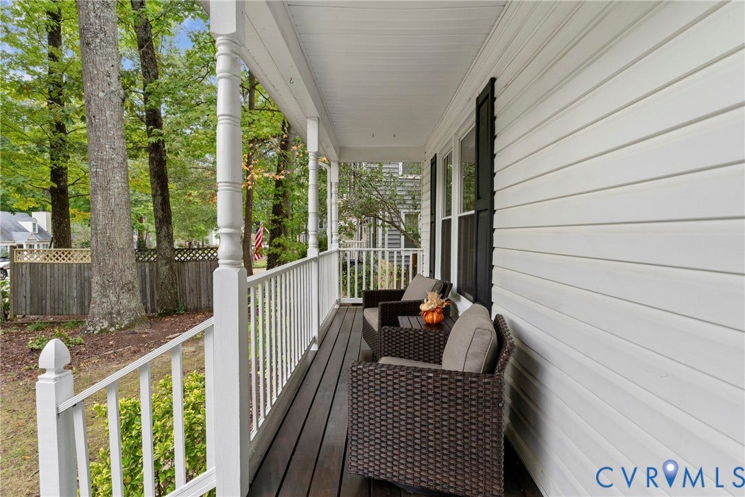 Covered front porch featuring white columns and railings, dark wood-finish flooring, and white horizontal siding with dark window shutters