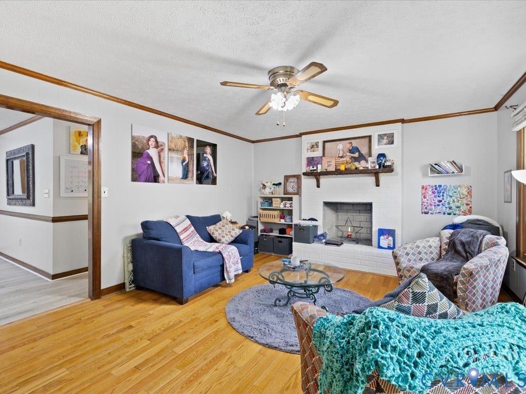 Hardwood flooring, painted brick fireplace with mantel, ceiling fan with integrated lighting, wood trim, and a cased opening