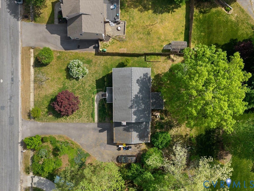 Shingle roof residence with an asphalt driveway, established landscaping, and mature trees