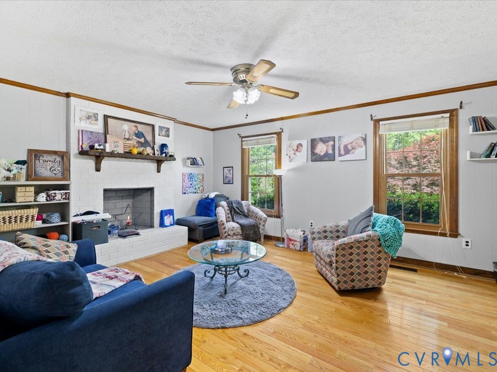 Hardwood flooring, white brick fireplace with mantel, ceiling fan with light fixture, large windows, built-in shelving