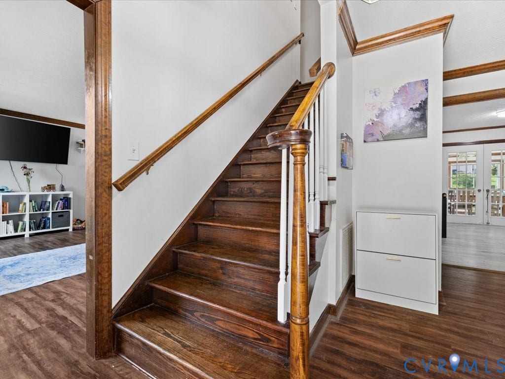 Wood-finish flooring throughout, dark wood staircase with white risers, wood newel post with white balusters, and transom window French doors