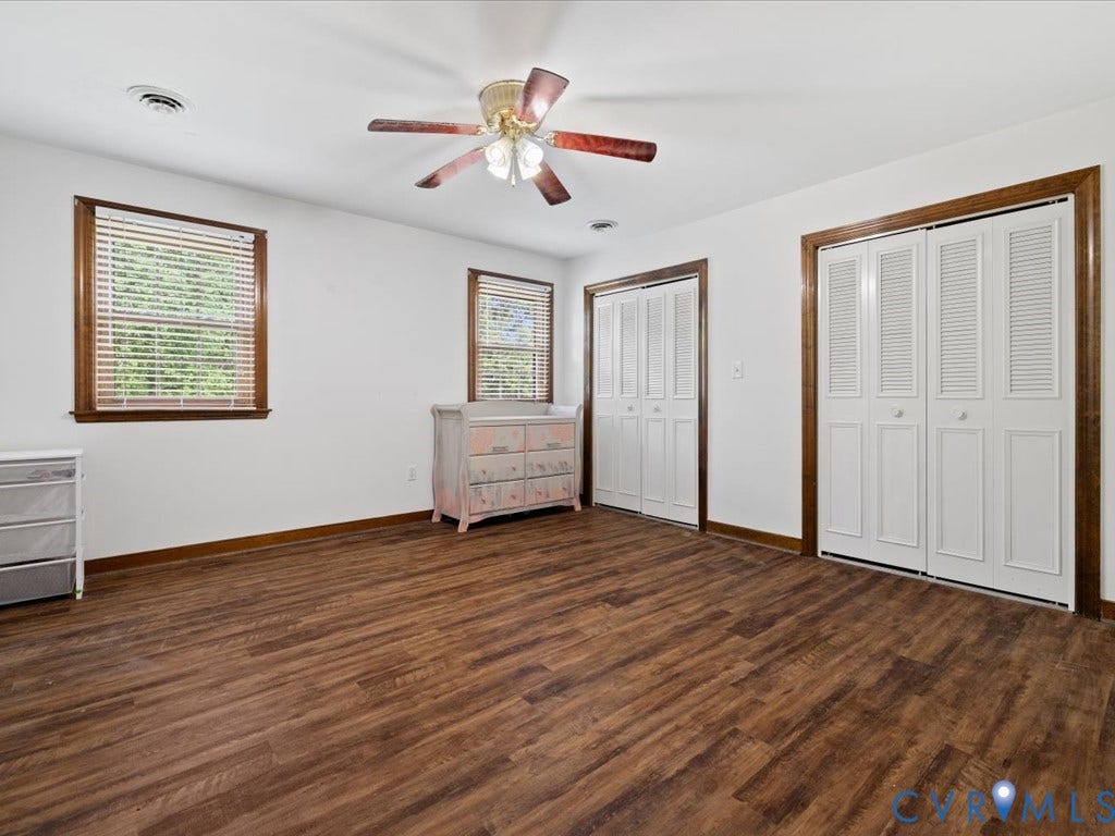 Wood-finish flooring, two windows with wood trim, built-in ceiling fan, and two bi-fold closet doors with wood trim