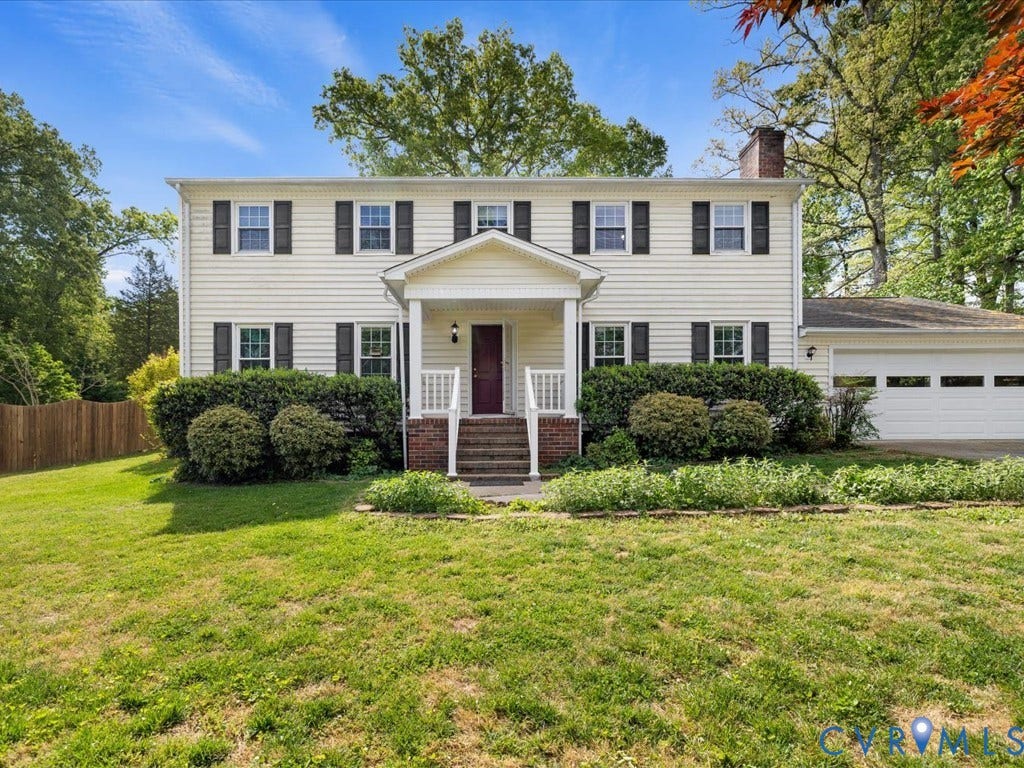 Traditional colonial-style exterior with light-colored siding, dark shutters, covered front entry, attached garage, and established landscaping