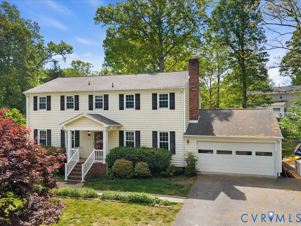 Two-story residence featuring light-colored siding, black window shutters, a covered front entry with white railings, an attached garage, and a brick chimney