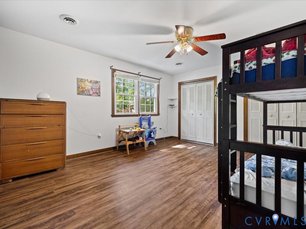 Wood-finish flooring, white walls, double windows with wood trim, ceiling fan, and bi-fold closet doors