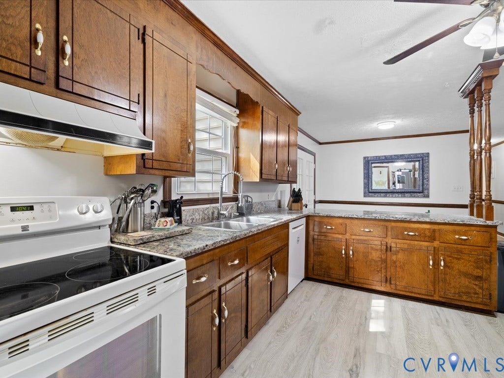 Wood-finish cabinetry with white hardware, light-toned countertops, stainless steel sink with gooseneck faucet, white built-in appliances, and light wood-finish flooring