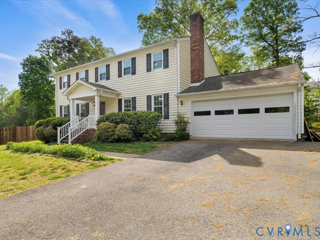 Traditional two-story residence featuring a covered front porch, a brick chimney, and a two-car garage with transom windows