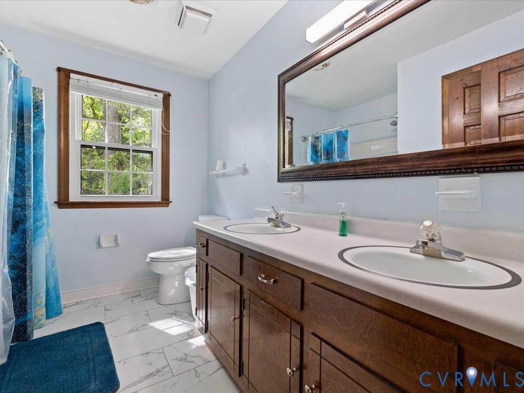 Dual vanity with integrated sinks, framed mirror, wood-finish cabinetry, and tiled flooring
