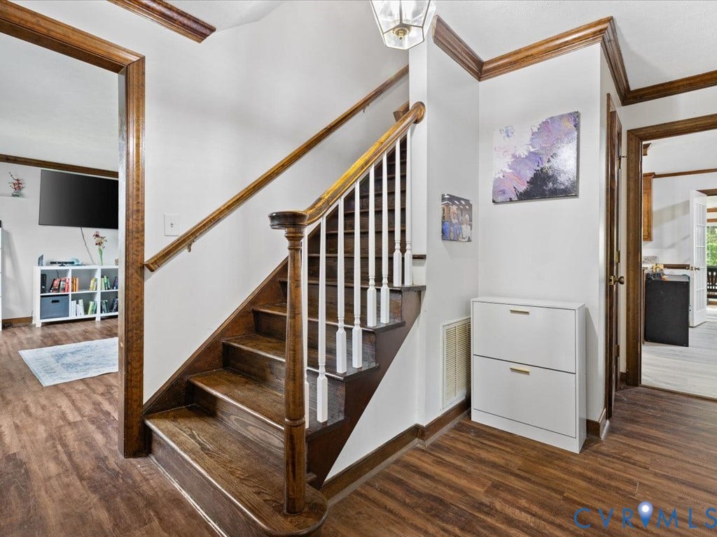 Wood-finish flooring throughout, solid wood staircase with white balusters, and crown molding accents