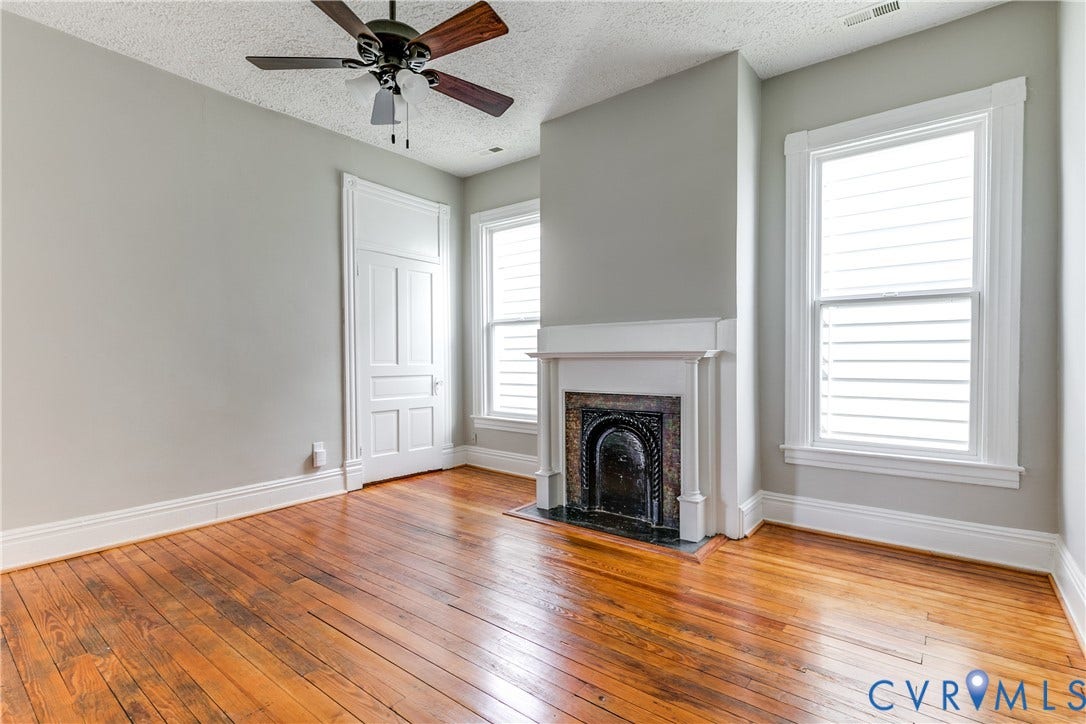 704 Chimborazo Boulevard, Chimborazo, Richmond, VA 23223 Wood-finish flooring, built-in fireplace with mantel, two windows with white louvered blinds, and a ceiling fan with light fixture