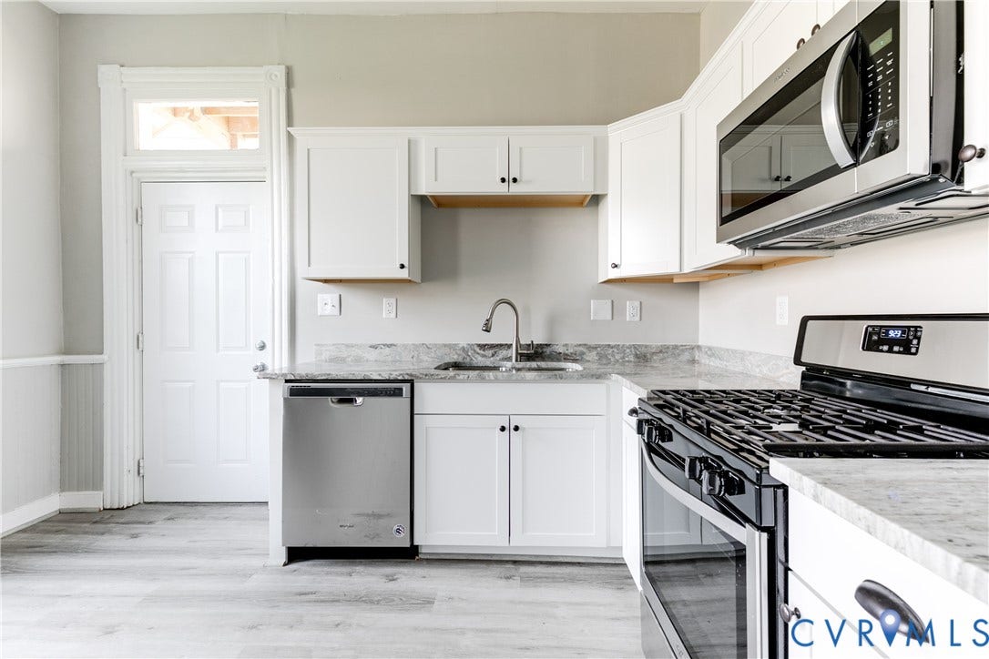 704 Chimborazo Boulevard, Chimborazo, Richmond, VA 23223 Kitchen featuring white cabinetry, stainless steel appliances, light-toned countertops, a sink with a chrome faucet, and wood-finish flooring