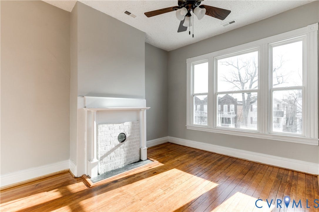 704 Chimborazo Boulevard, Chimborazo, Richmond, VA 23223 Hardwood flooring, painted brick fireplace with white mantel, wide window trim, ceiling fan, and painted walls