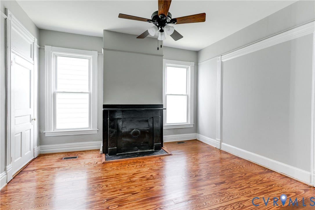 704 Chimborazo Boulevard, Chimborazo, Richmond, VA 23223 Hardwood flooring, two windows, ceiling fan, fireplace with dark mantel, and white trim details