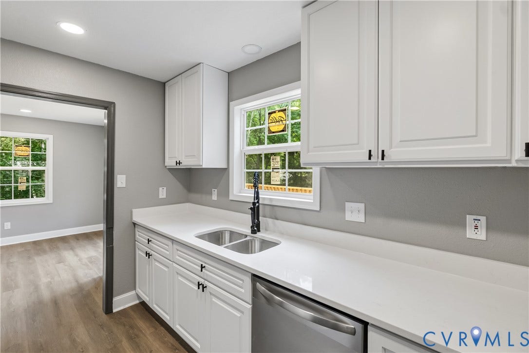 White shaker cabinetry with dark hardware, stainless steel sink with a matte black faucet, durable white countertops, and wood-finish flooring