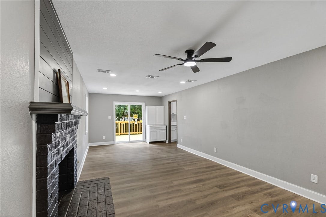 Wood-finish flooring with a brick fireplace, integrated ceiling fan, recessed lighting, and sliding glass doors to outdoor decking