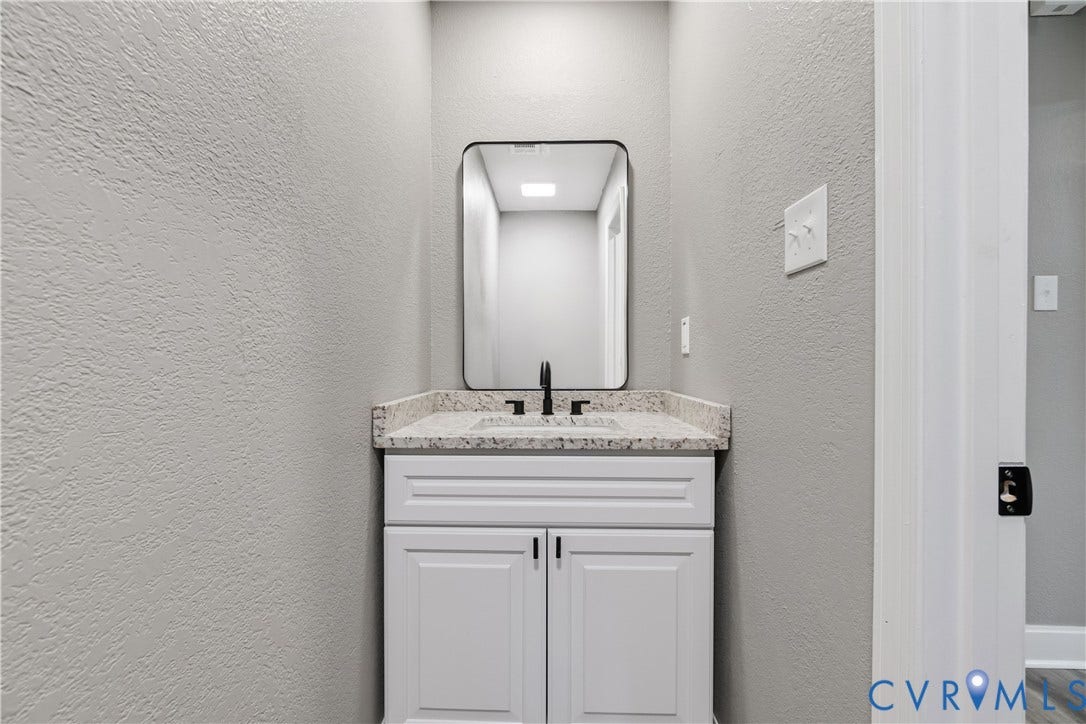White vanity with dark hardware, stone countertop, undermount sink, matte black faucet, and a rectangular framed mirror