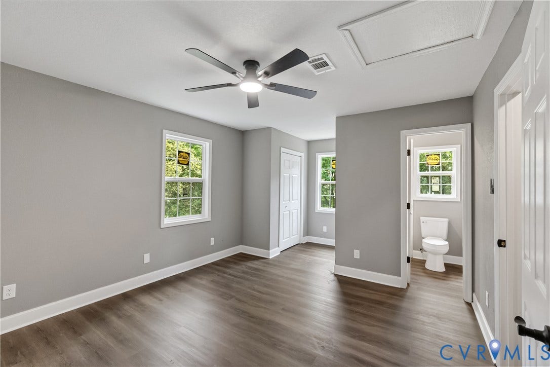 Spacious room featuring wood-finish flooring, light gray walls, multiple windows, and an attached ceiling fan with lighting