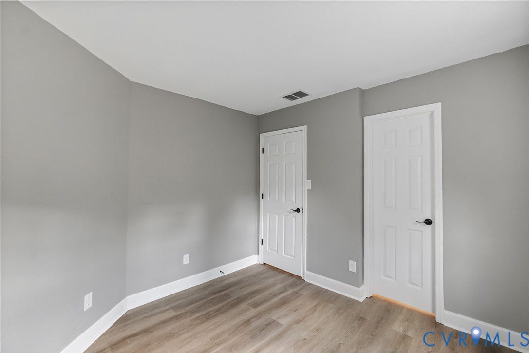 Light gray wall paint, white trim, wood-finish flooring, two paneled doors, and black door hardware