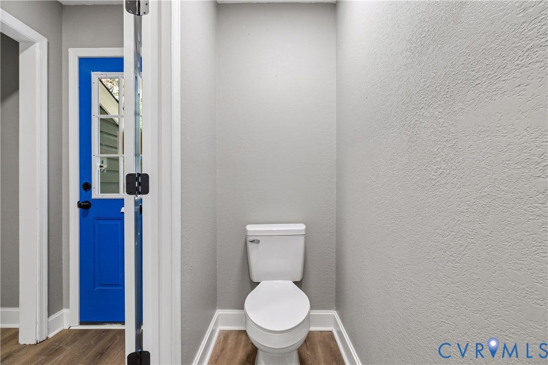 White toilet fixture, wood-finish flooring, white trim, and a blue paneled door