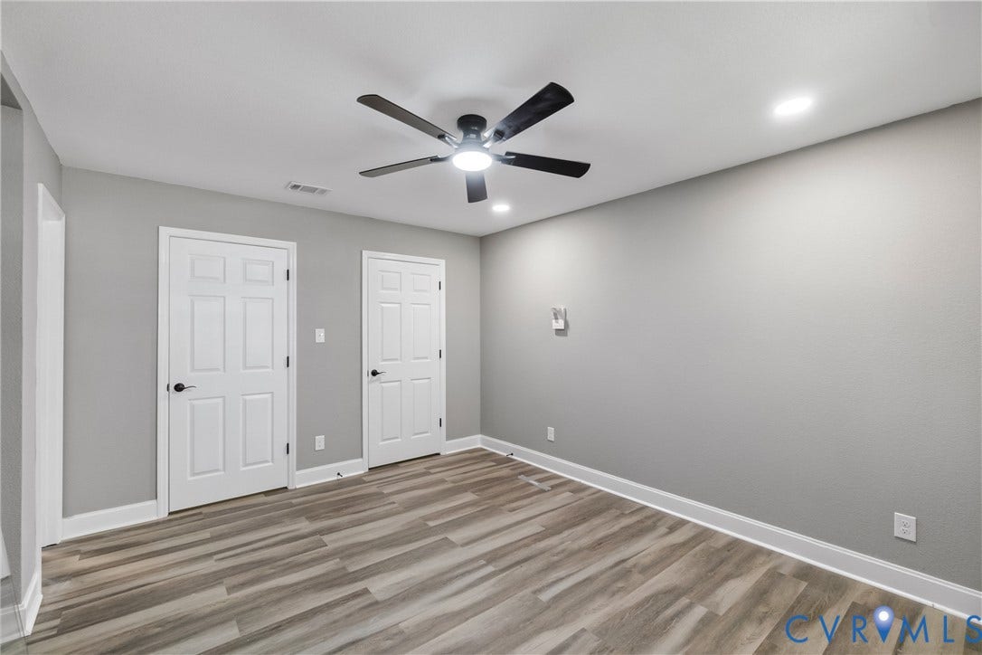 Wood-finish flooring, two paneled doors with black hardware, recessed ceiling lighting, and a ceiling fan with integrated lighting