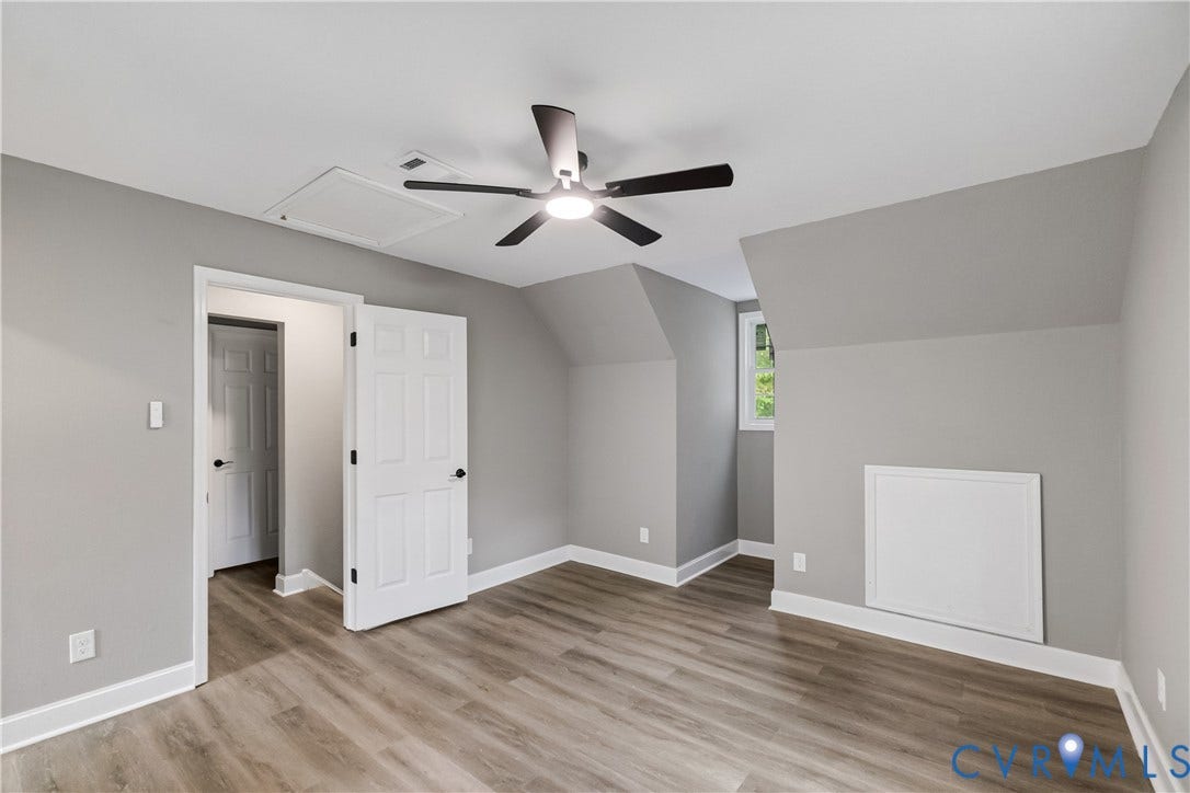 Spacious bedroom with neutral gray walls, wood-finish flooring, and ceiling fan with integrated lighting