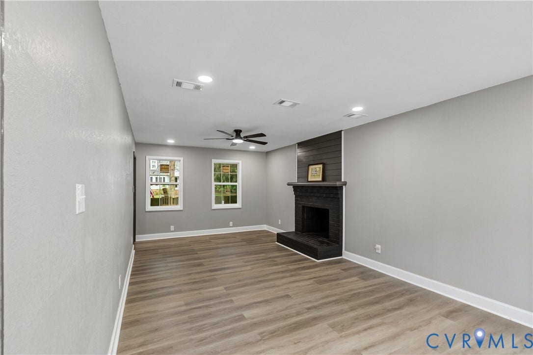 Spacious interior featuring wood-finish flooring, a contemporary ceiling fan, recessed lighting, and a dark brick fireplace with shiplap detailing