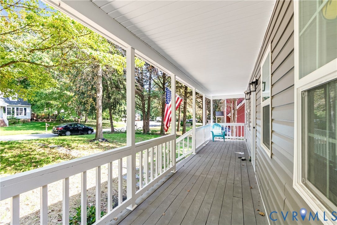Covered front porch with a white railing and gray composite decking, featuring gray siding and multiple windows