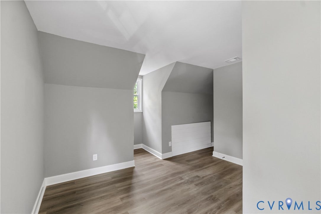 Wood-finish flooring, neutral wall tones, window, and sloped ceiling details