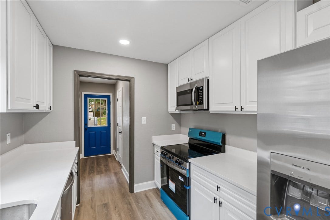 White cabinetry with matte black hardware, stainless steel appliances, wood-finish flooring, and light-toned countertops