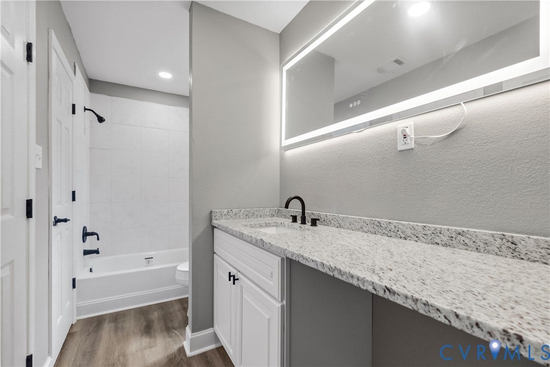 White vanity with matte black hardware, stone-finish countertop, undermount sink, and integrated lighted mirror