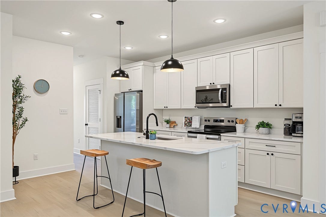 Light wood-finish flooring, white cabinetry with black hardware, stainless steel appliances, a kitchen island with seating, and recessed lighting