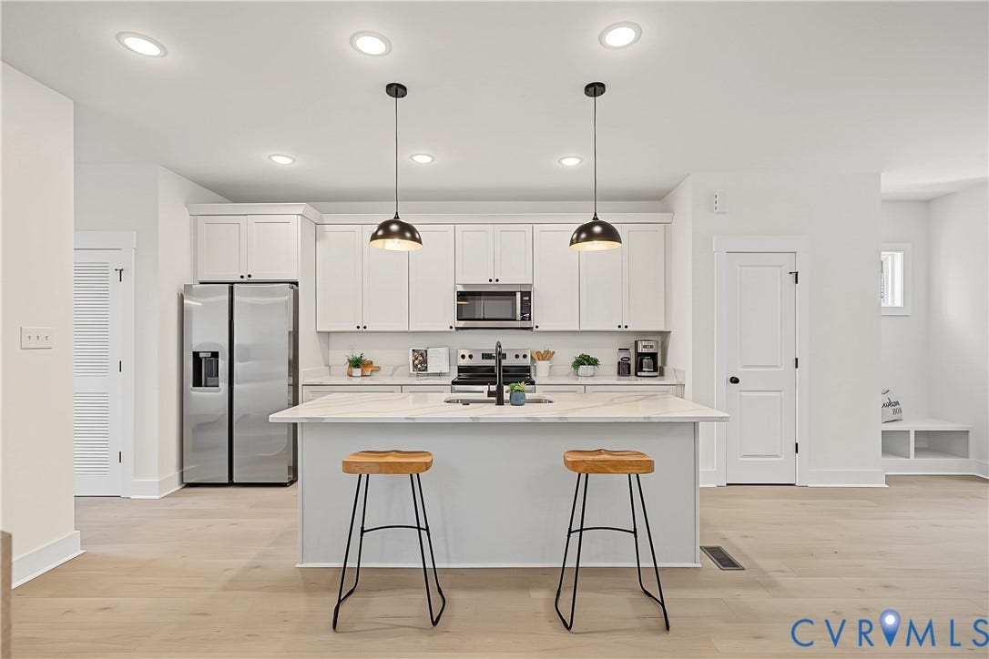 Contemporary kitchen featuring white cabinetry, a center island with pendant lighting, stainless steel appliances, and light wood-finish flooring