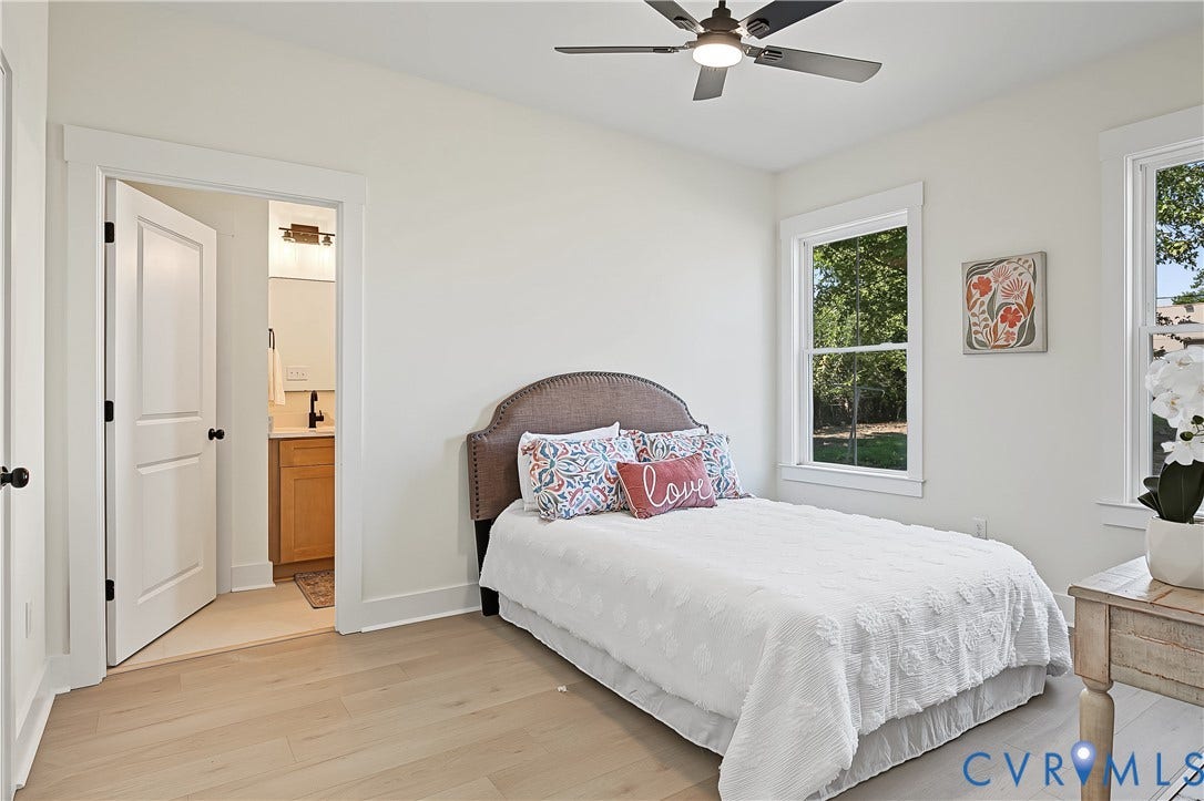Light wood-finish flooring, two windows with white trim, and a ceiling fan with integrated lighting