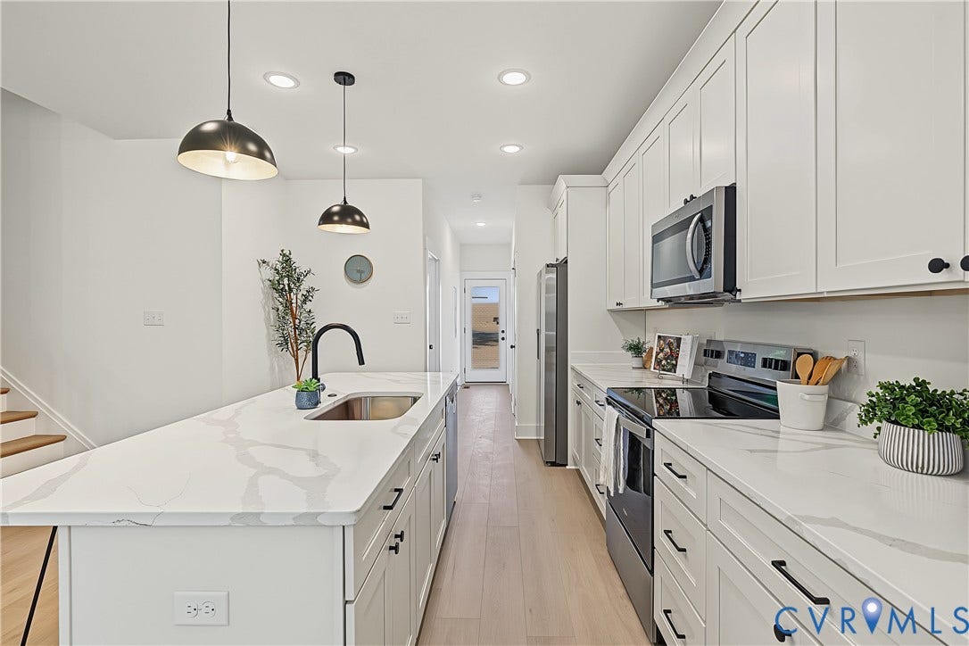 Kitchen featuring white shaker-style cabinetry, stainless steel appliances, light wood-finish flooring, and pendant lighting