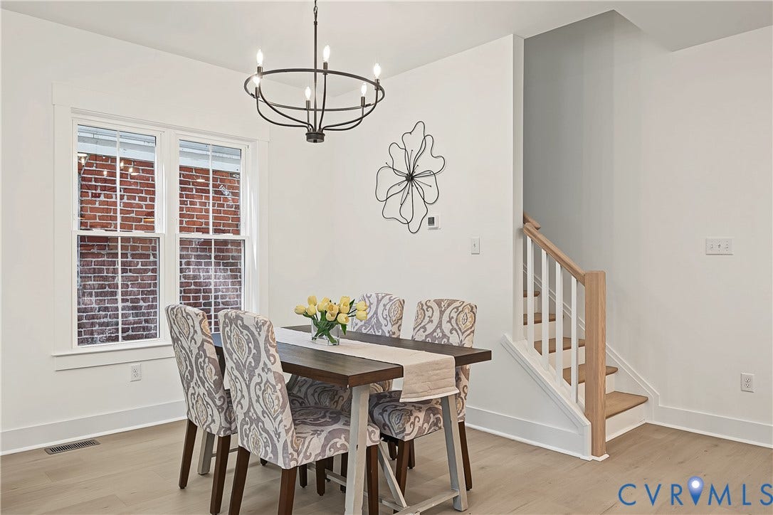 White walls with wide baseboards, black metal chandelier, light wood-finish flooring, and a staircase featuring wood treads and a white railing
