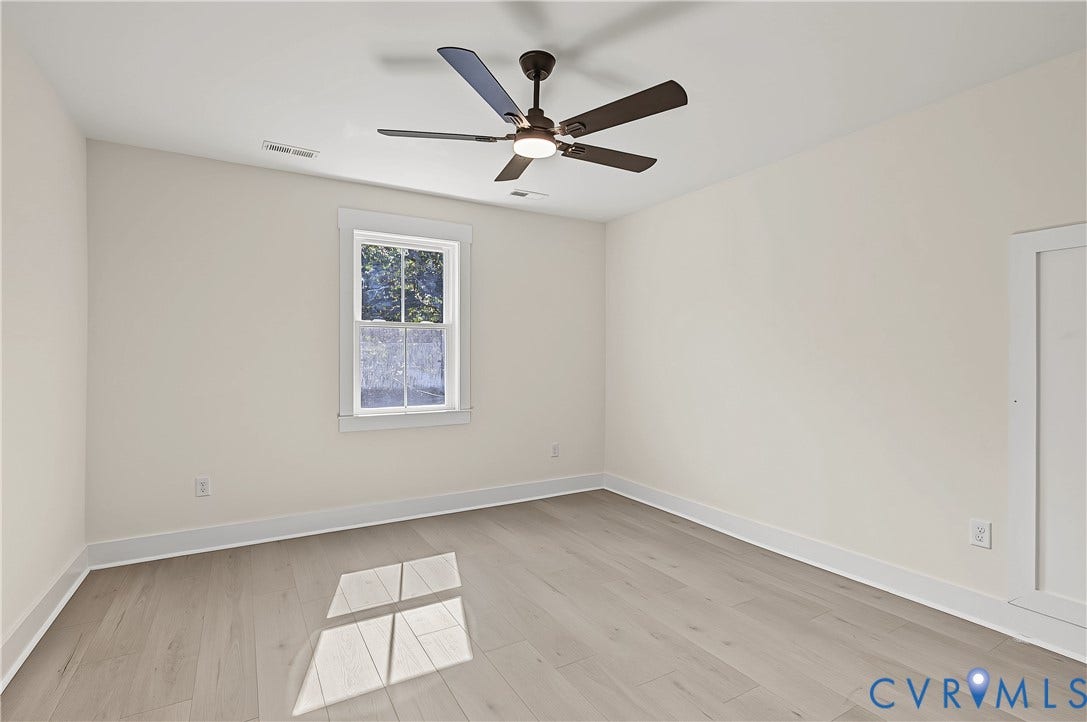 Wood-finish flooring, single window with white trim, ceiling fan, white baseboards, and a white door with trim