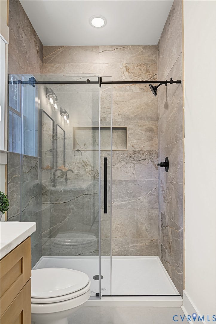 Walk-in shower featuring a sliding glass door, tiled walls, a built-in shower niche, and matte black fixtures