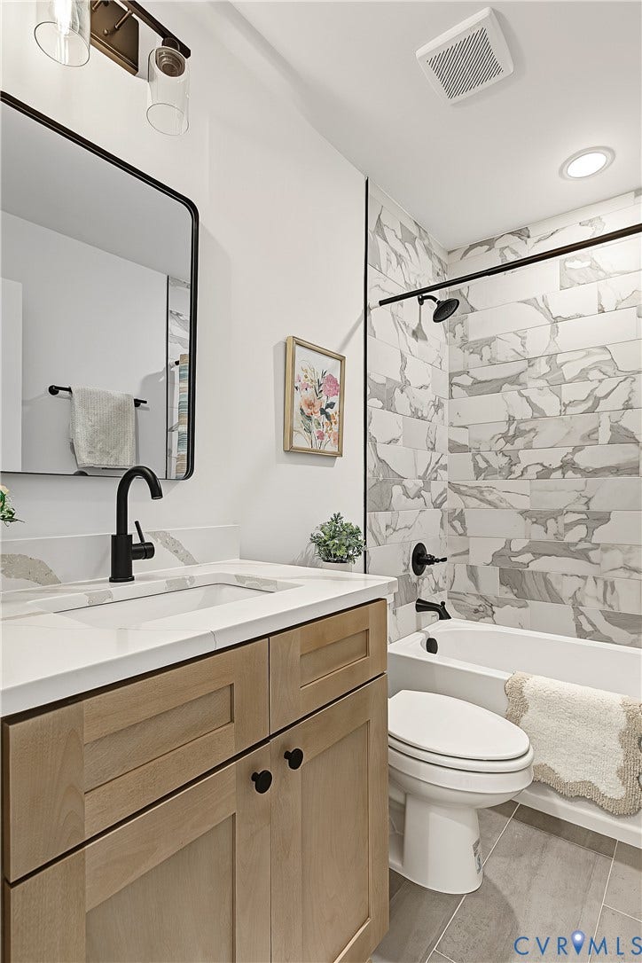 Bathroom featuring a wood-finish vanity, white countertop, rectangular undermount sink, black fixtures, and a tiled shower-tub combination