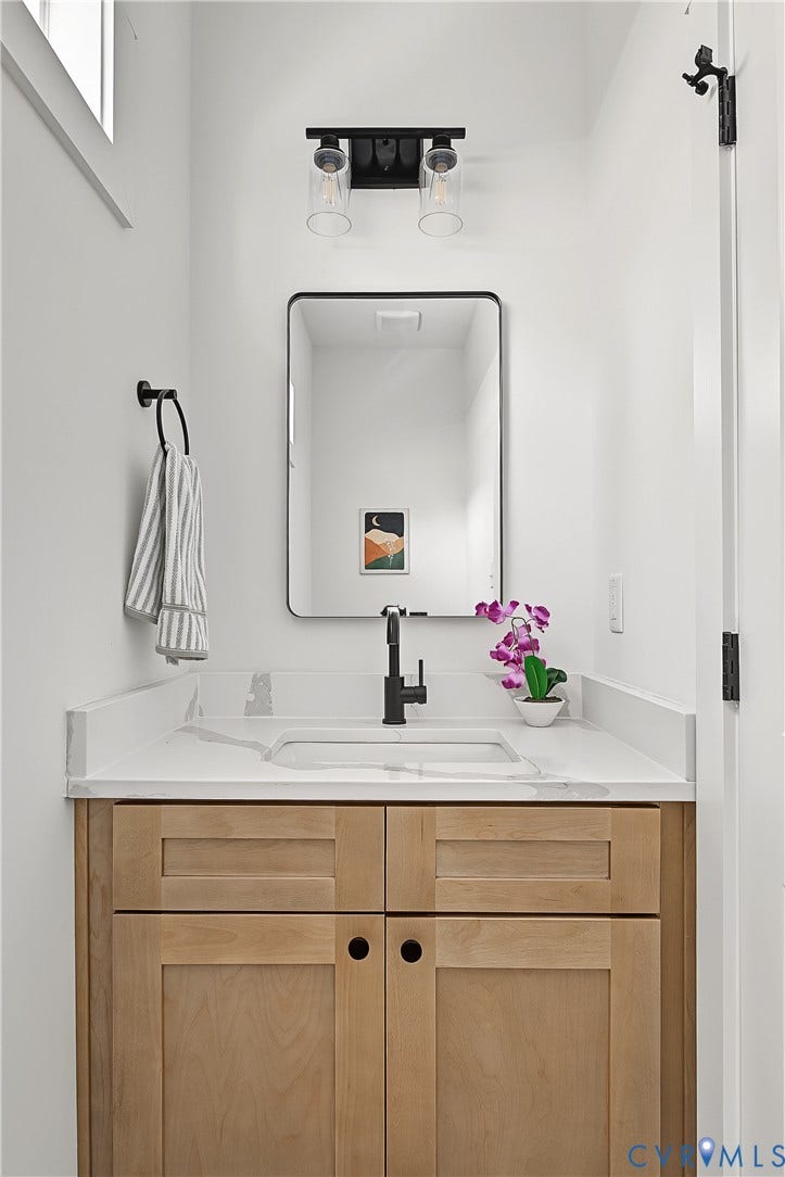 Light wood-finish vanity with an integrated sink and white countertop, complemented by a matte black faucet