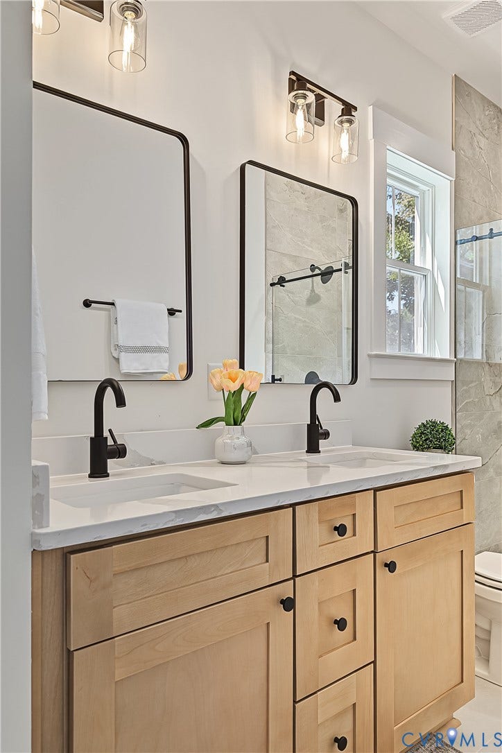 Dual vanity with light wood-finish cabinetry, white countertop, and matte black fixtures