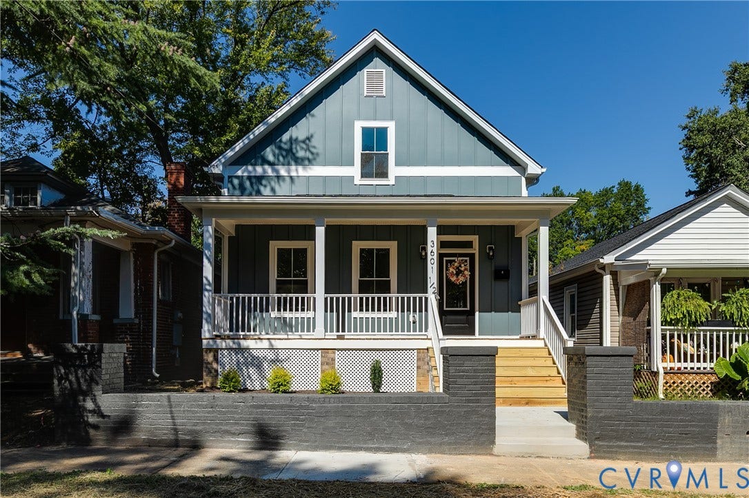 Expansive front porch with white railings, natural wood stairs, and dark brick pillars