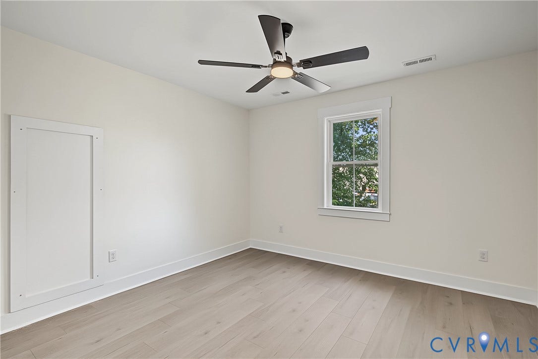 Light wood-finish flooring, a ceiling fan with integrated lighting, a double-hung window with white trim, and white baseboards