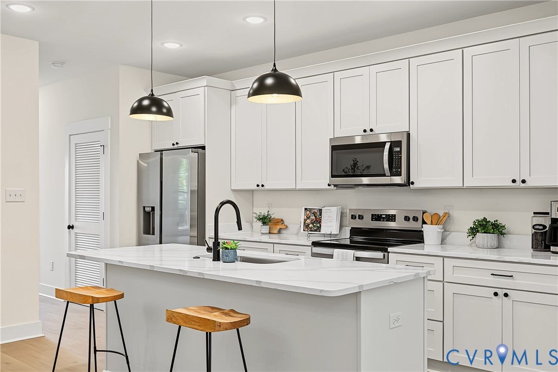 Kitchen featuring an island with an undermount sink, white shaker cabinetry, stainless steel appliances, and pendant lighting