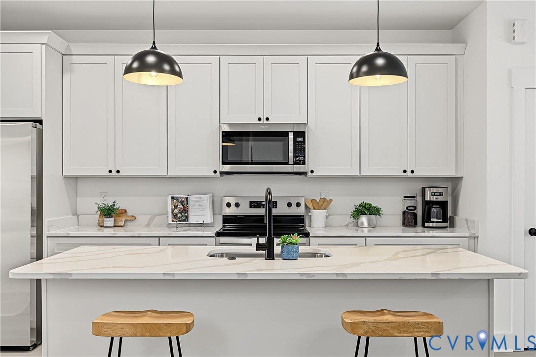 Contemporary kitchen featuring white cabinetry, a large kitchen island with an integrated sink, stainless steel appliances, and pendant lighting
