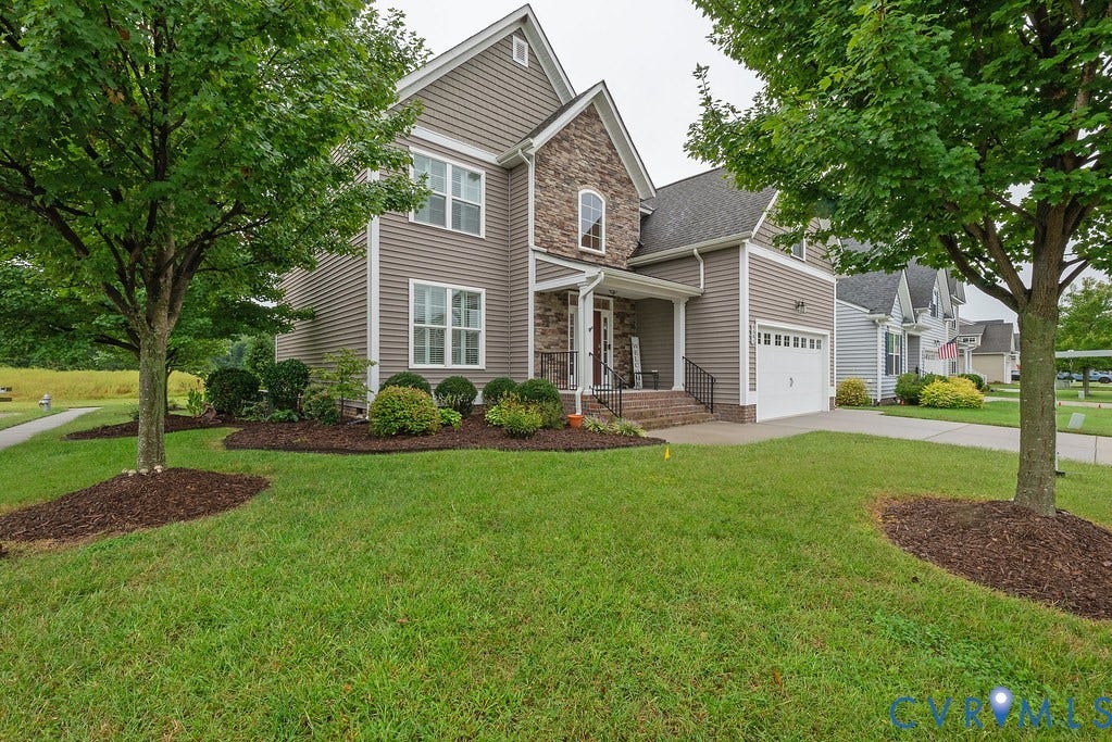 6301 Broad Sky Circle, Quiet, Mechanicsville, VA 23111 Exterior featuring horizontal siding, stone veneer accents, an attached garage with a white door, a covered entry porch, and mature landscaping