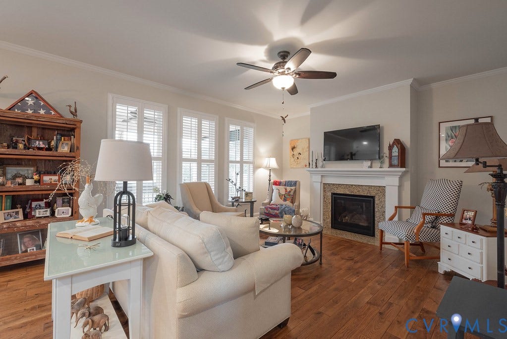 6301 Broad Sky Circle, Quiet, Mechanicsville, VA 23111 Hardwood flooring, fireplace with stone surround and white mantel, multiple windows with white plantation shutters, white crown molding, and a ceiling fan with integrated lighting