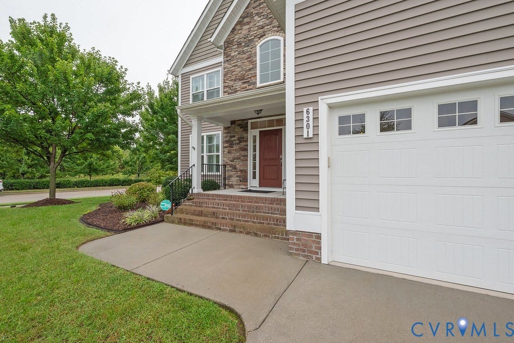 6301 Broad Sky Circle, Quiet, Mechanicsville, VA 23111 Two-car garage with transom windows, stone faade accents, covered porch with white columns, brick steps, and a red front door